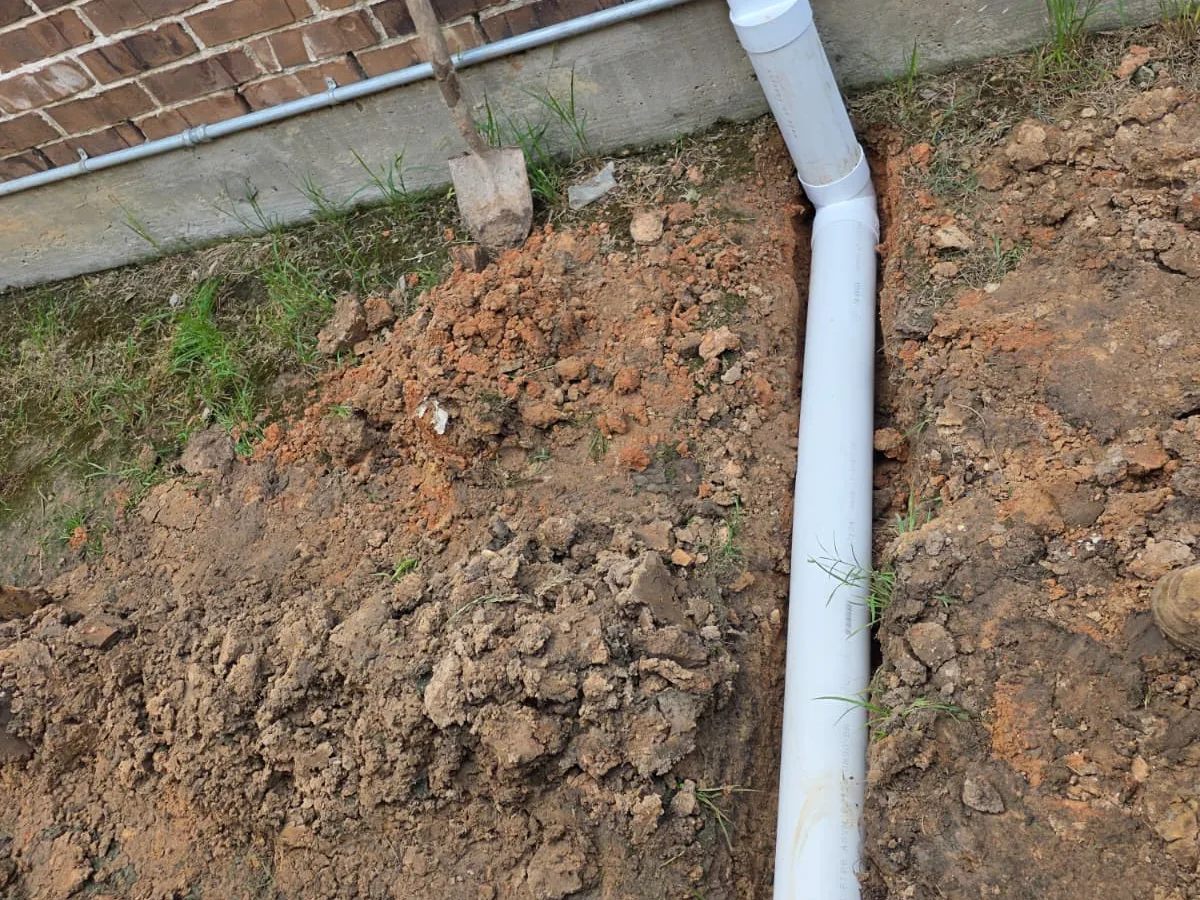 Downspout drain pipe trenched along a brick house foundation