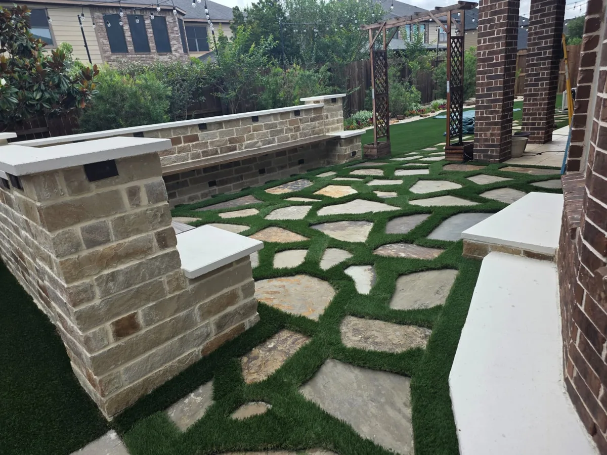Flagstone patio set in artificial turf beside a stone seating wall