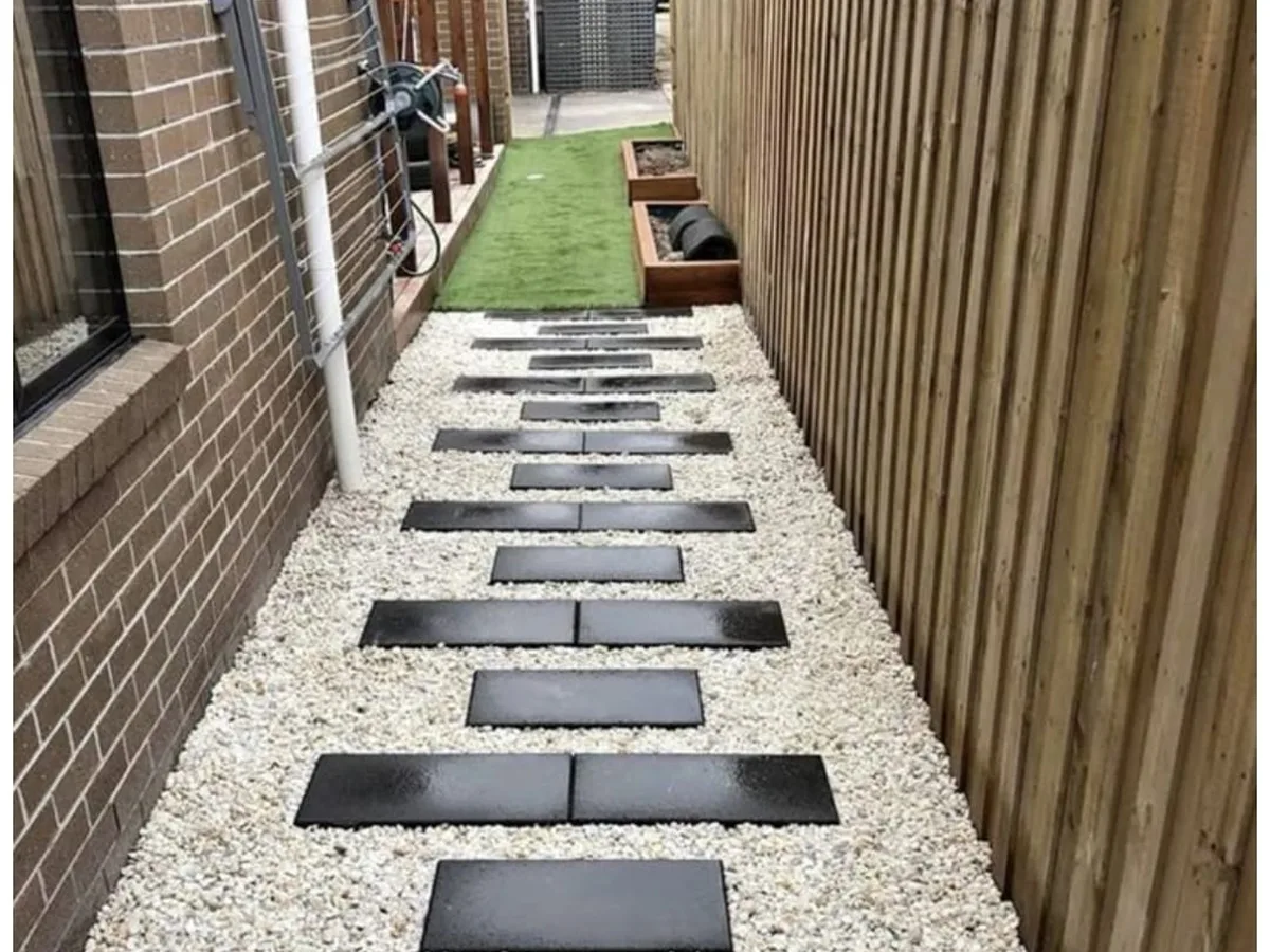 Dark stepping pads in white gravel along a wood fence