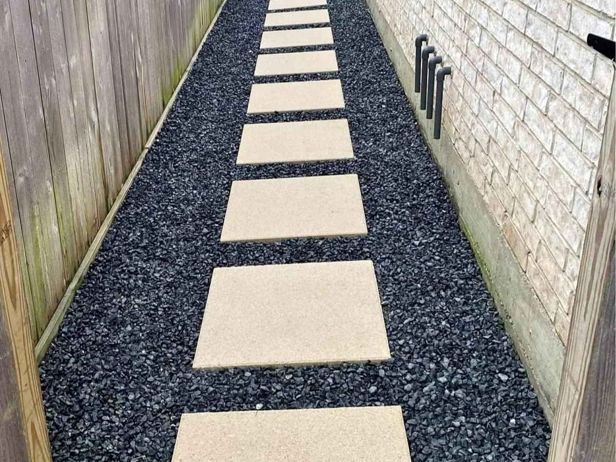 Side-yard walkway of concrete pads in dark gravel