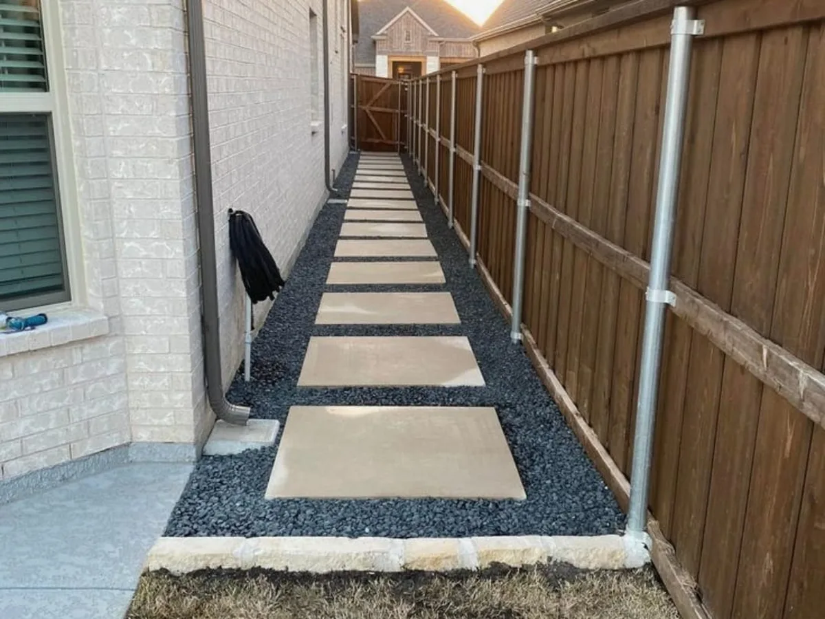 Concrete pads in gravel beside a new fence and house wall